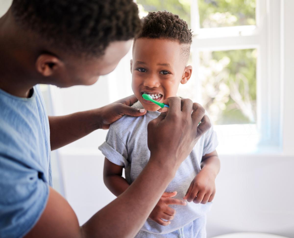 A father brushing his toddler son's teeth in the bathroom at home