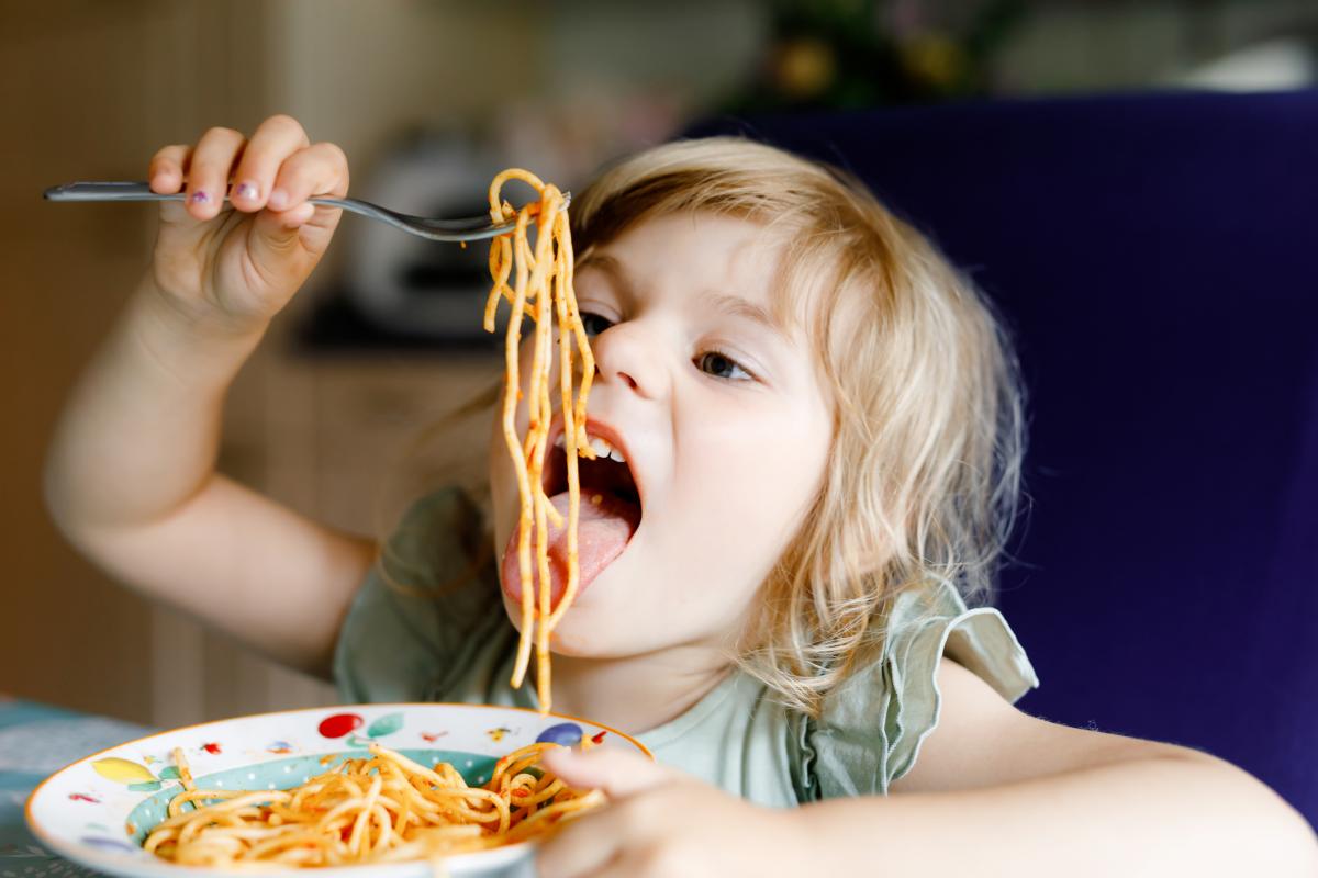 Little girl eating a plate of spaghetti. Holding up her fork draped with noodles about to take a big bite.