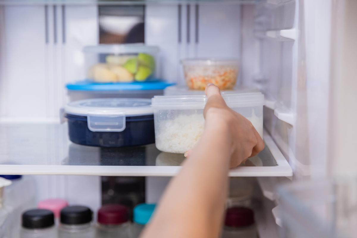 A view of someone's hand placing a container of food into the refrigerator.