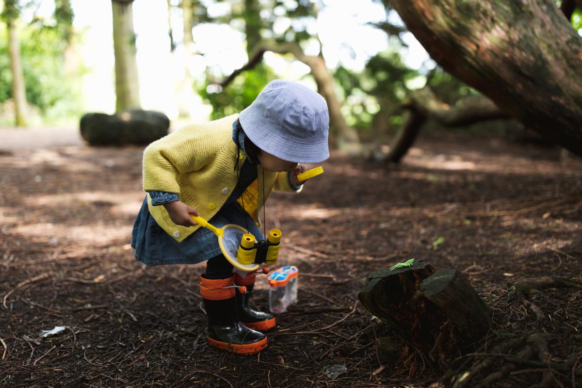 little girl in the forest, bending down to take a closer look at something with a magnifying glass