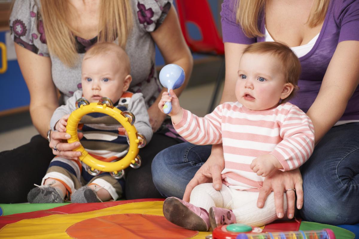 two babies sitting with their mothers playing musical instruments