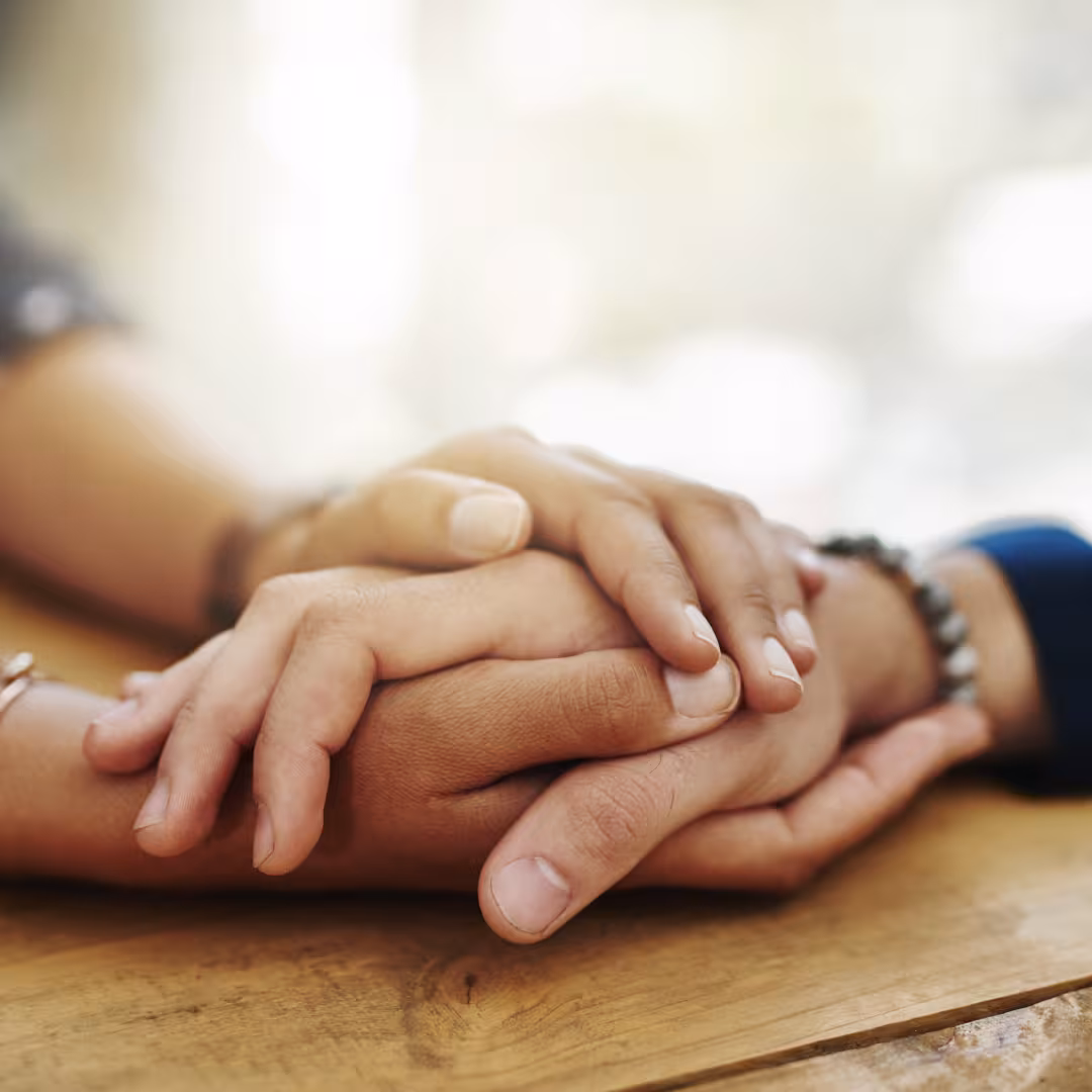 two people's hands shown on a table holding hands and providing comfort