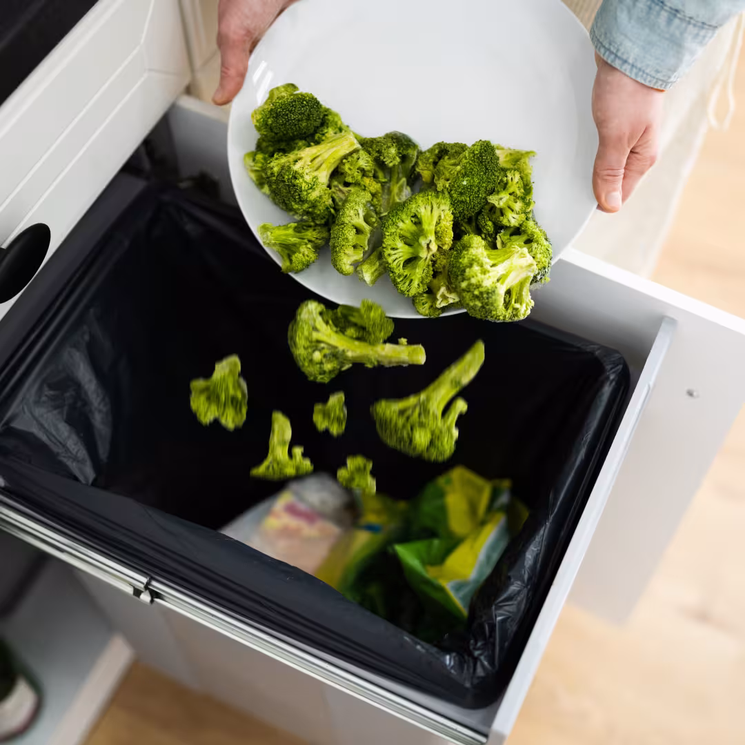 a plate of broccoli being scraped into the garbage