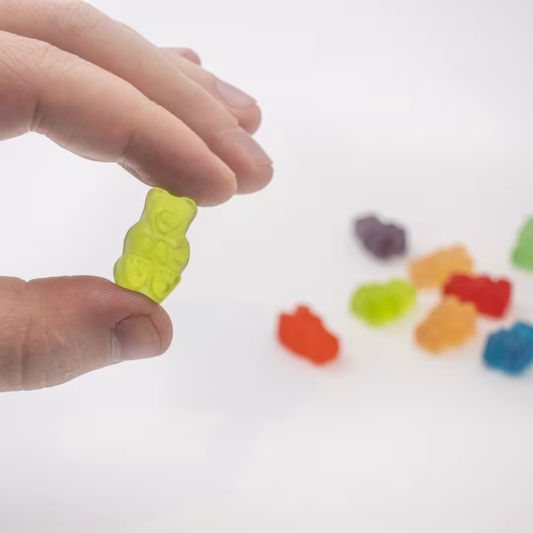 hand holding gummy bear candy with more candies sitting on the table behind