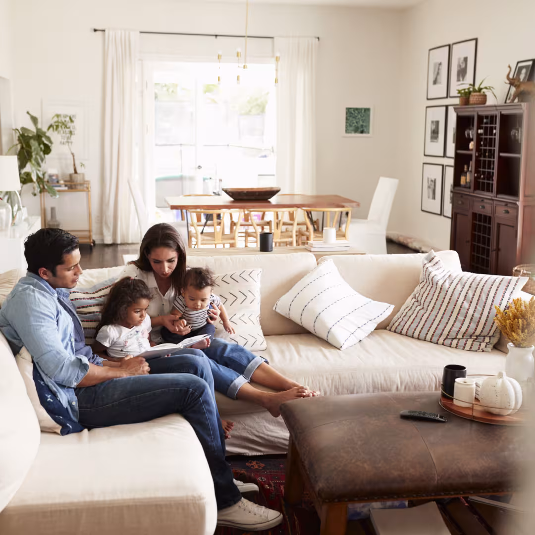  family sitting on sofa reading a book together in the living room, seen from doorway
