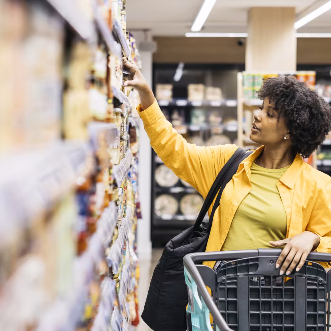 Woman pushing a grocery cart reaching for something on the shelf