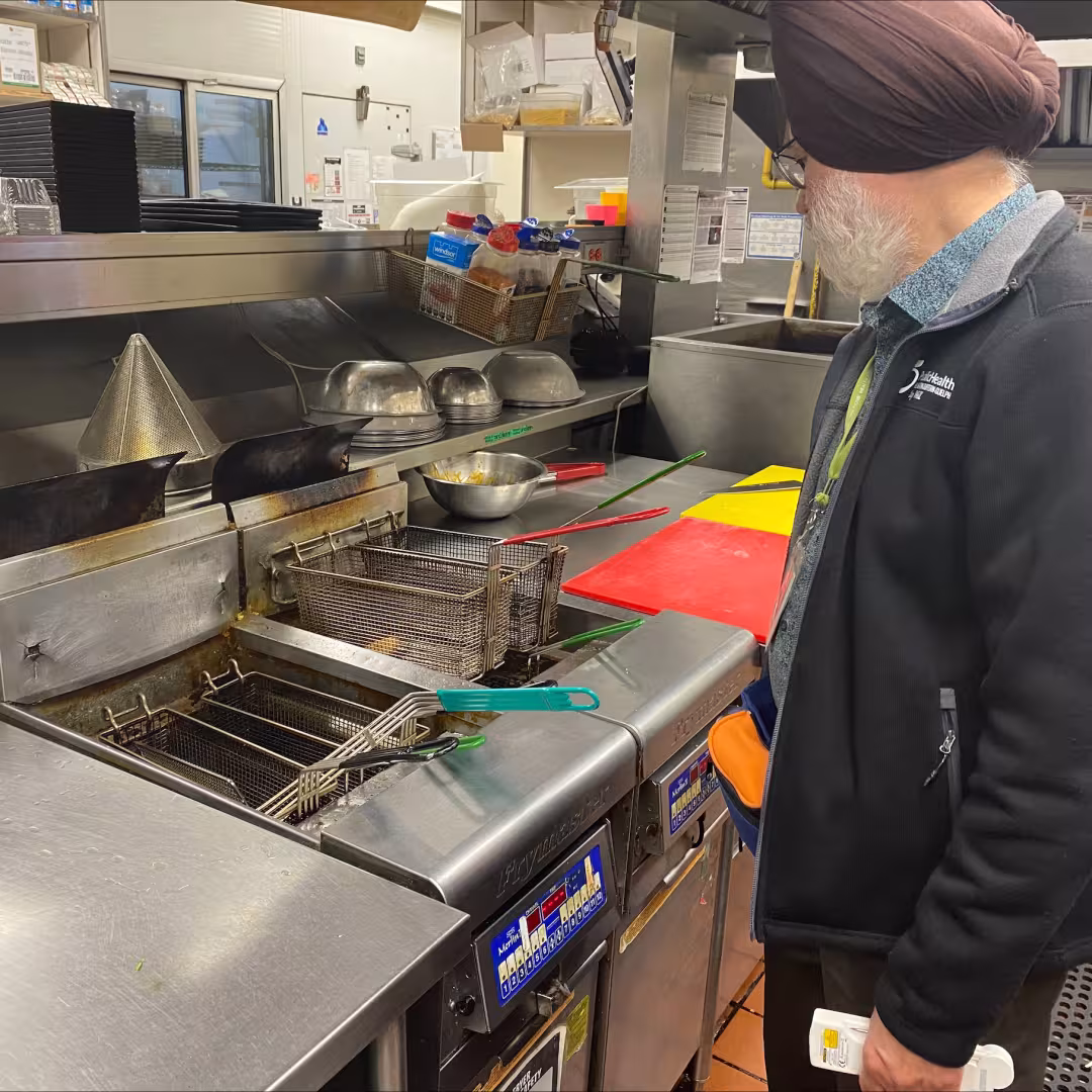 A public health inspector looks over deep fryers in a restaurant kitchen.
