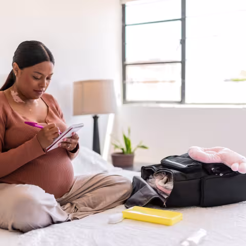 oung pregnant packing the baby clothes and maternity items on backpack at home 