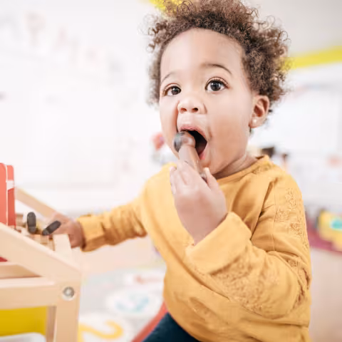Adorable toddler indoor of a classroom putting something in his mouth