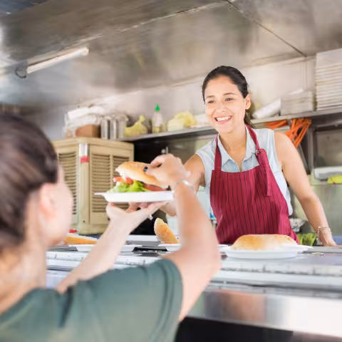Portrait of a gorgeous young woman working in a food truck and selling hamburgers with a smile