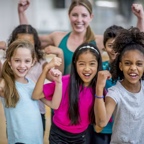 A group of elementary school students are posing with their teacher during gym class. 
