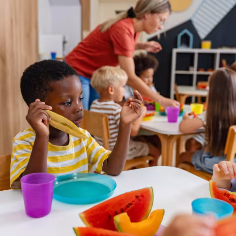 Preschool children sitting at a table eating fresh watermelon slices during snack time