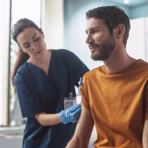 Happy Caucasian Man Sitting In The Chair In Bright Hospital And Getting His Hepatitis B Vaccine.