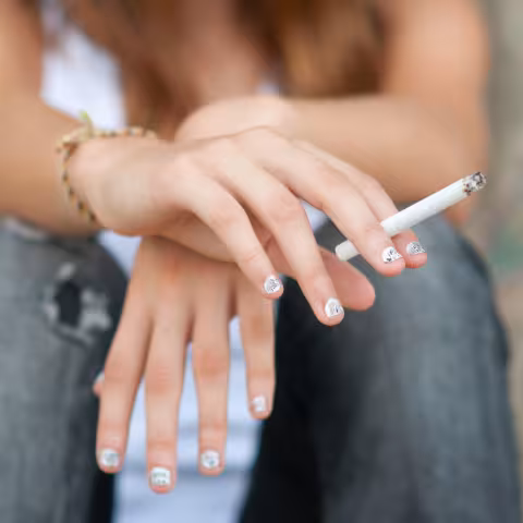 Teenage girl smoking cigarette while sitting on the street.