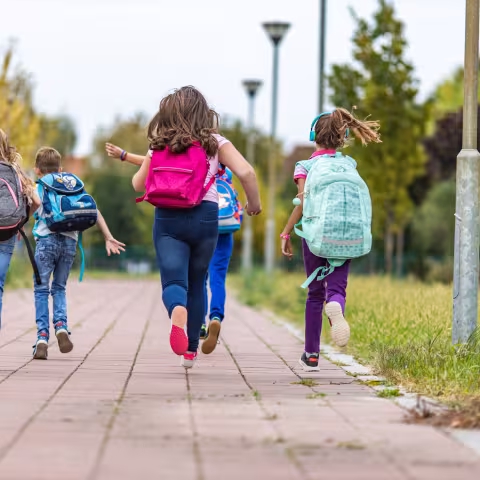 School children wearing backpacks running with their backs turned to the camera.