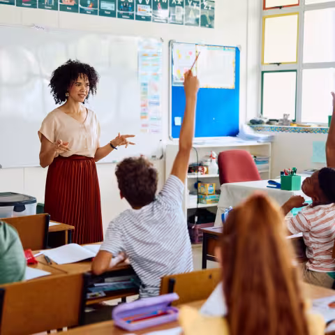 Elementary school teacher asking question, enthusiastic children with hands up 