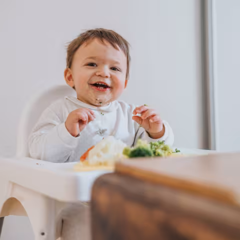 Baby eating vegetables in high chair