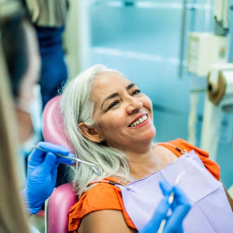 Happy senior woman at dental clinic looking at camera. Her dentist is in the background.