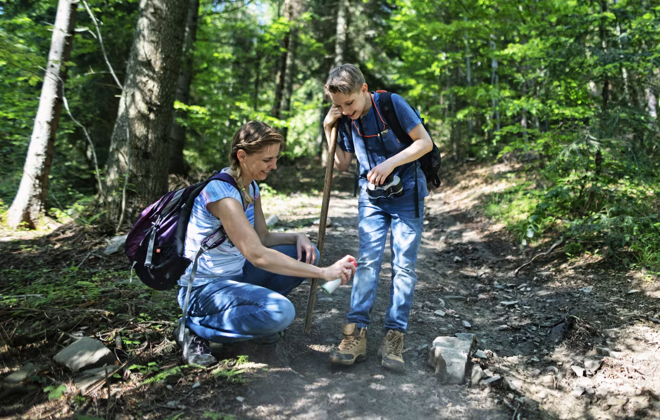 woman spraying her son with insect repellent on a hike on a trail