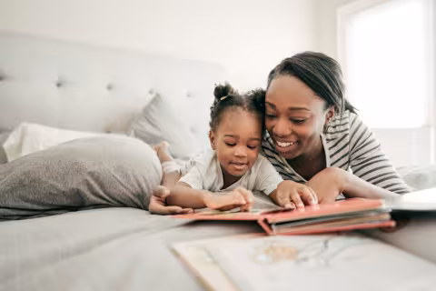 mother and toddler lay on the bed together reading a book