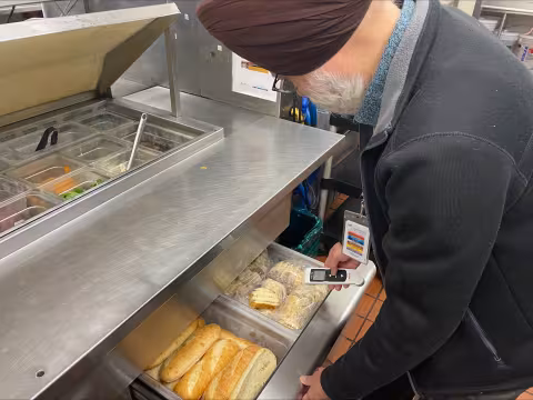 A public health inspector in a restaurant kitchen checks food holding temperatures with a thermometer.