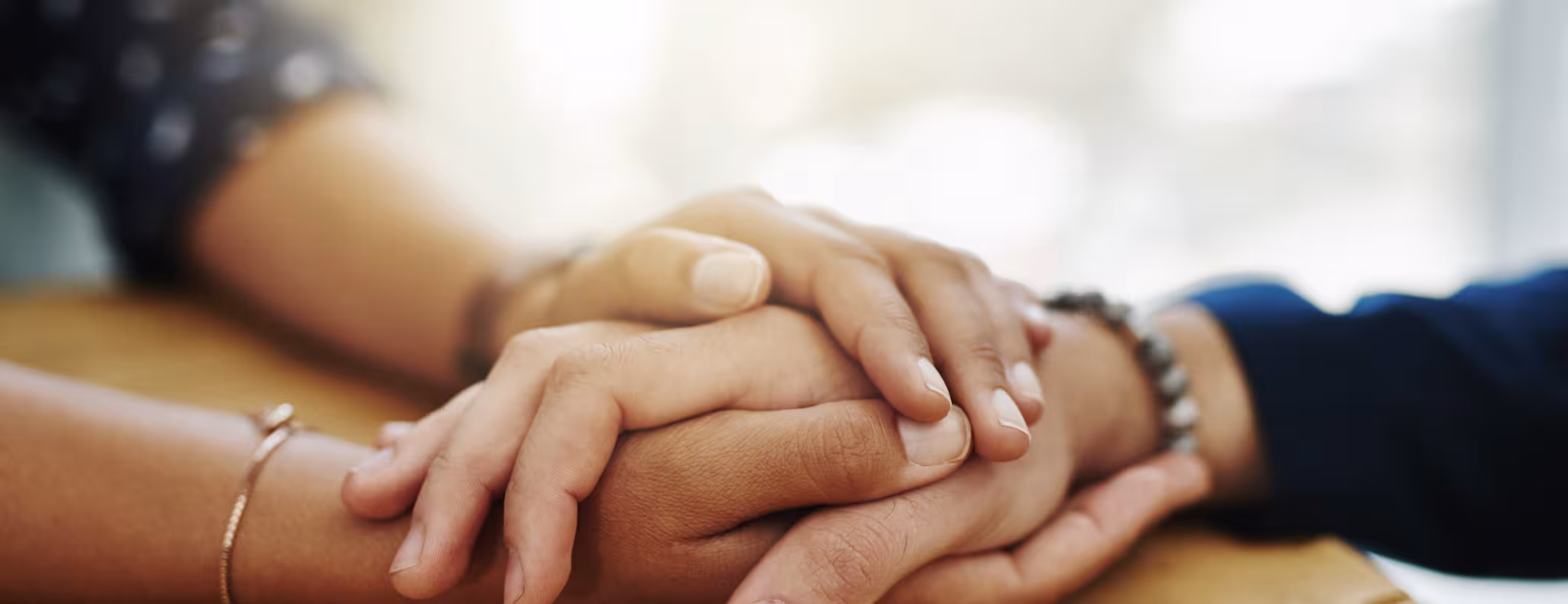 two people's hands shown on a table holding hands and providing comfort