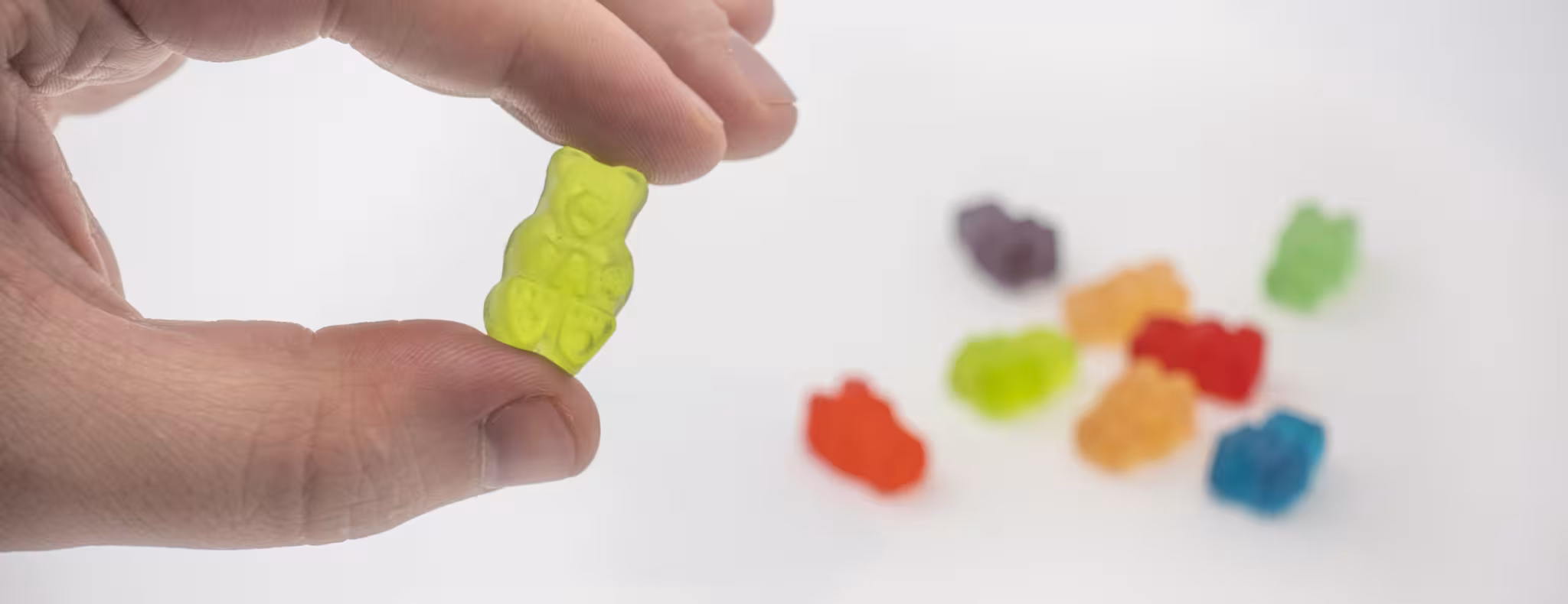 hand holding gummy bear candy with more candies sitting on the table behind