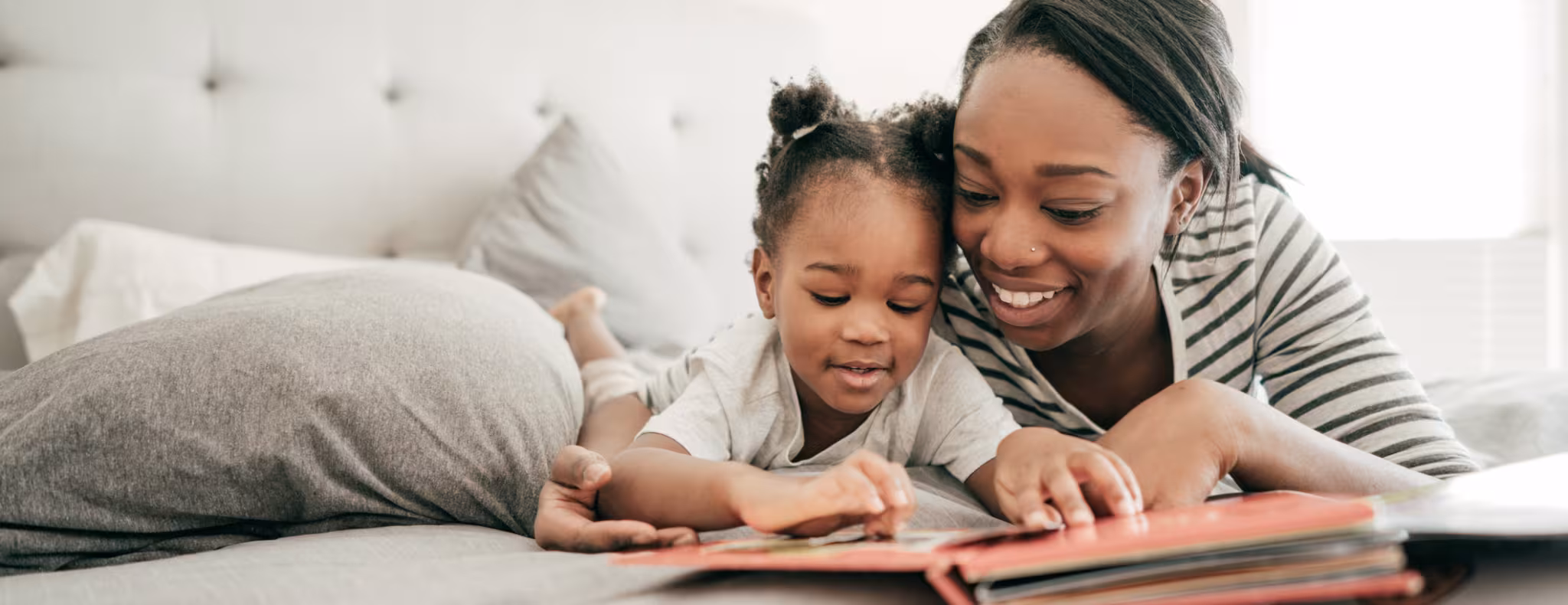 mother and toddler lay on the bed together reading a book