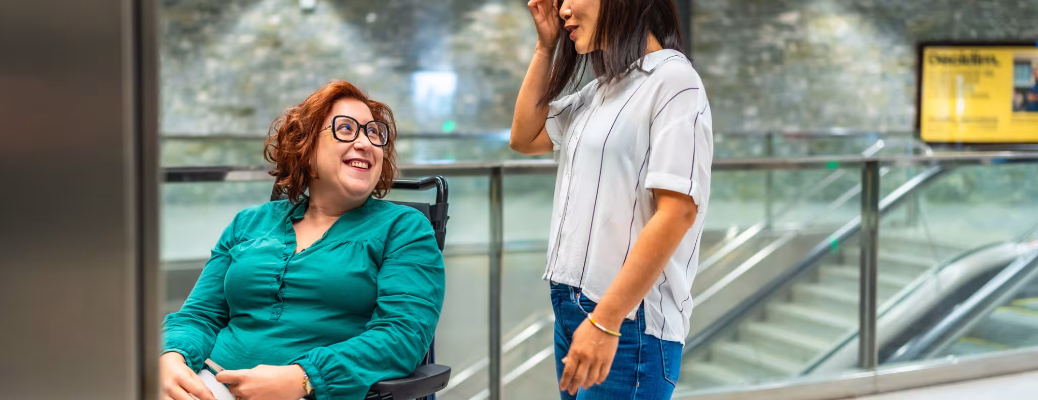 Smiling woman in a wheelchair and support worker talking waiting for elevator.