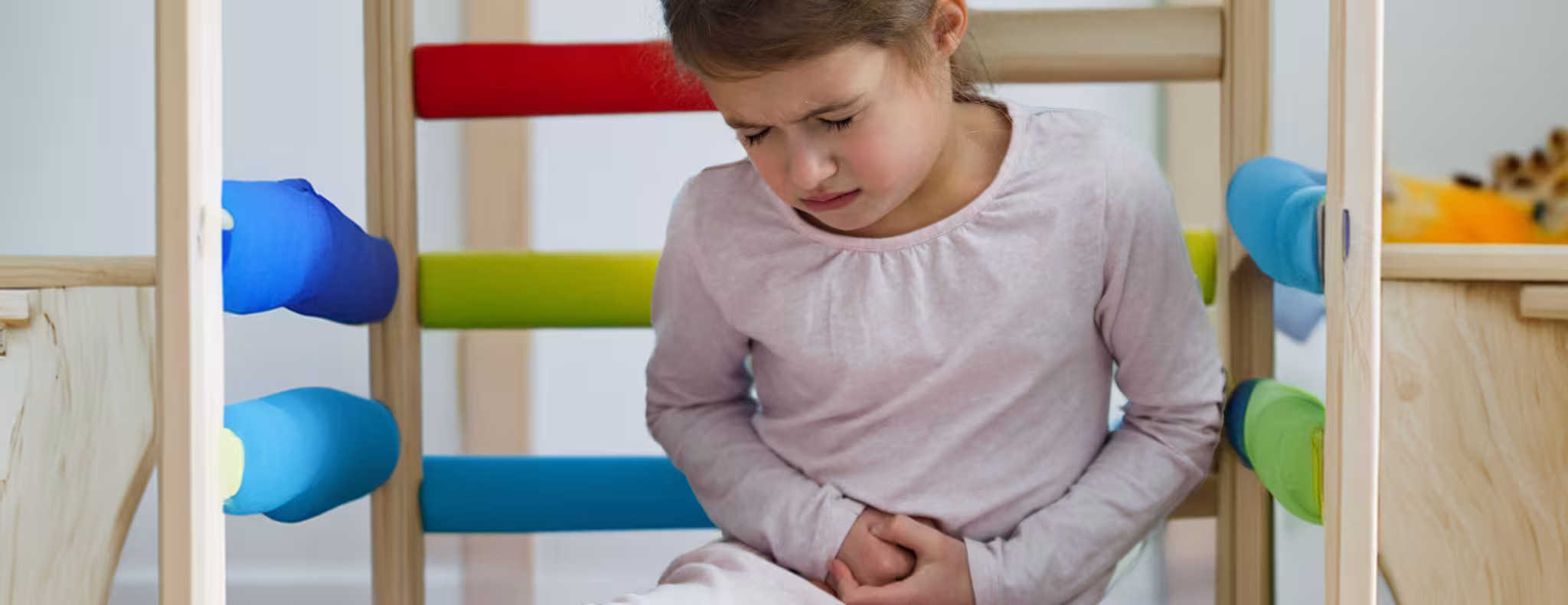 Child sitting in a play structure at daycare with stomach pain