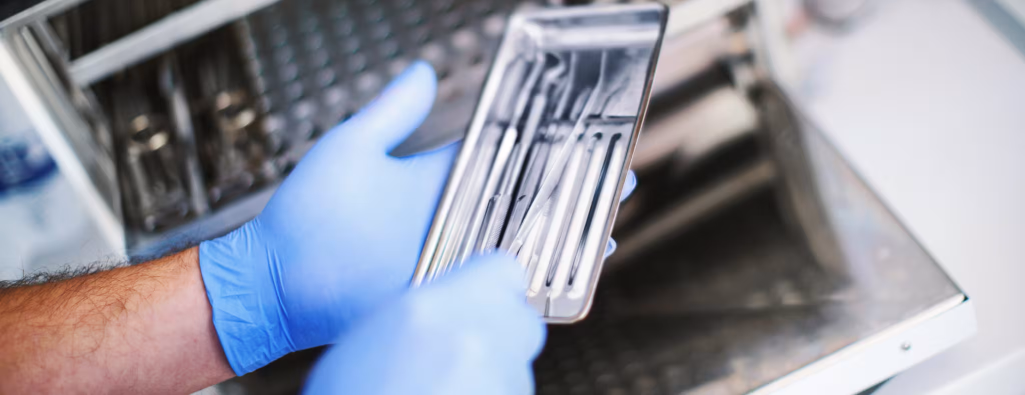 Unrecognizable male dental technician picking dental instruments from a sterilizer for a basic dental set up.
