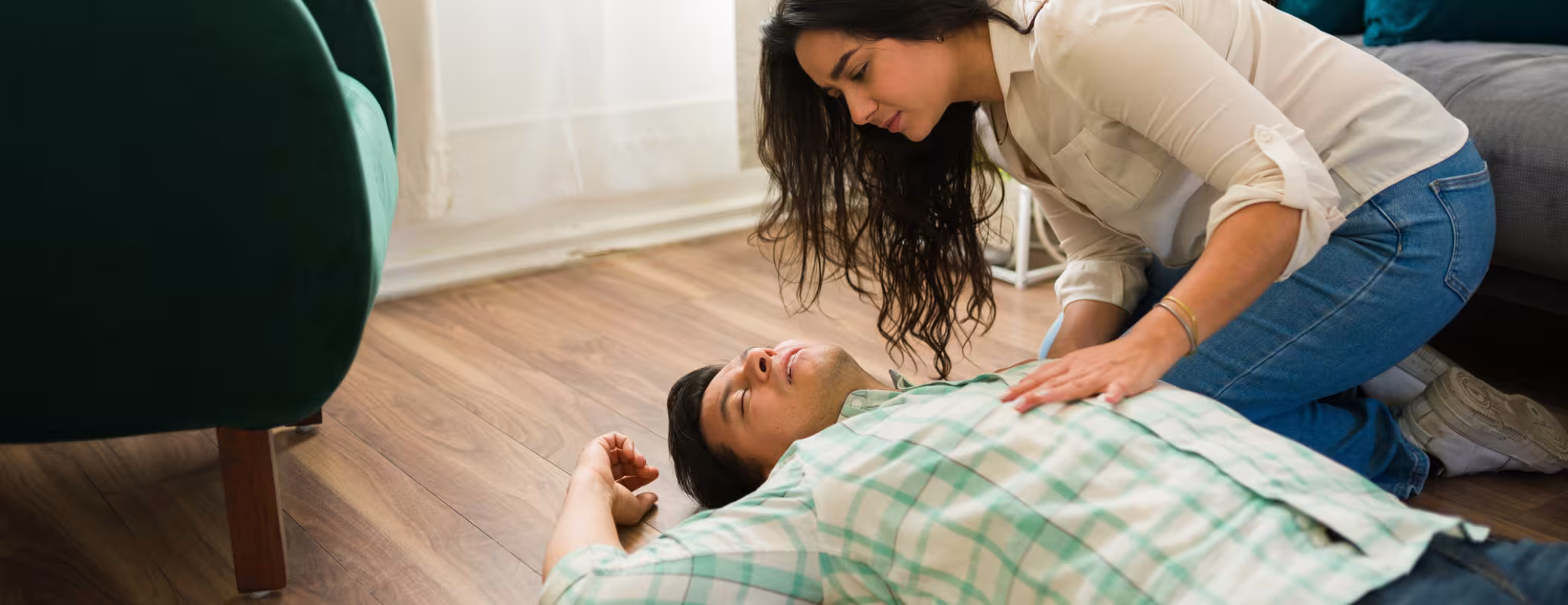 Woman providing emergency first aid, kneeling beside unconscious partner, checking vital signs in residential setting