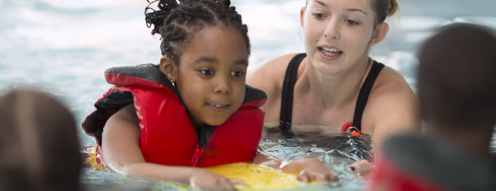 A multi-ethnic group of elementary age children are learning how to swim at the public pool. 