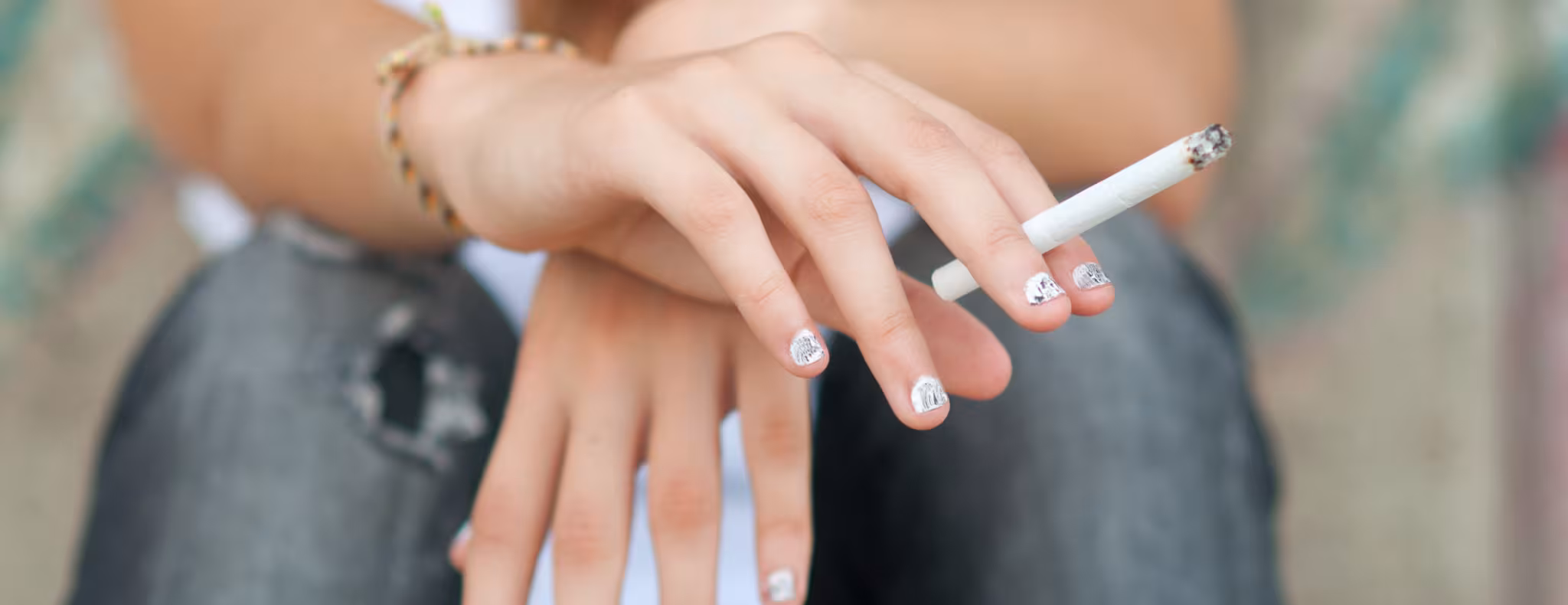 Teenage girl smoking cigarette while sitting on the street.