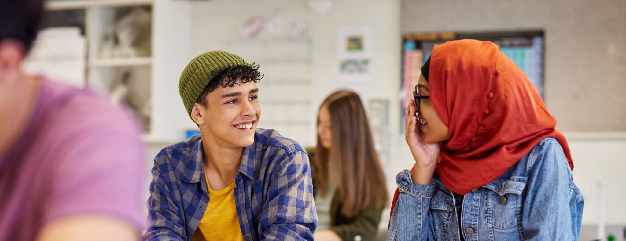 Two students smiling and talking happily during lesson at secondary school. 