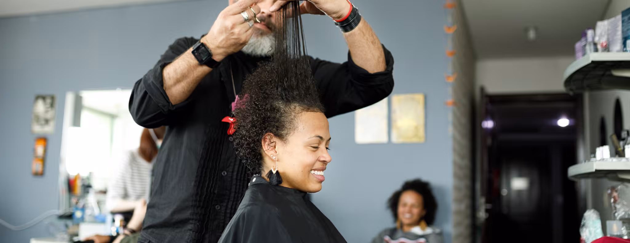 Male hairdresser combing hair up to do haircut for smiling woman