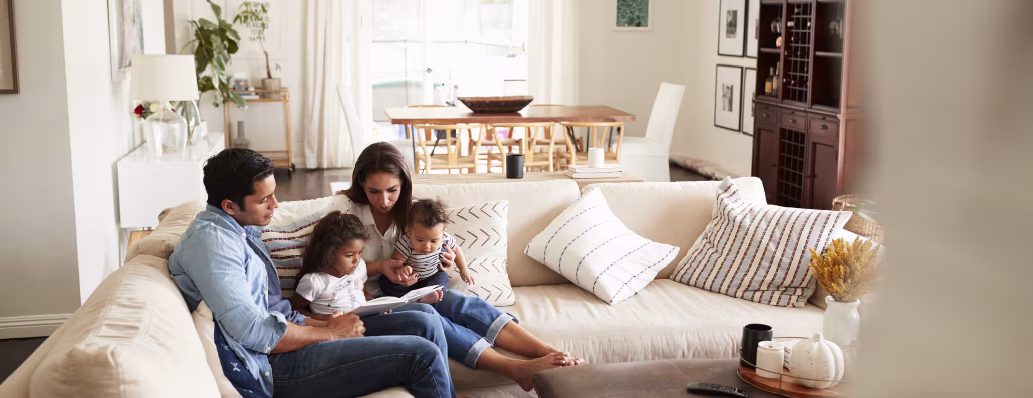  family sitting on sofa reading a book together in the living room, seen from doorway