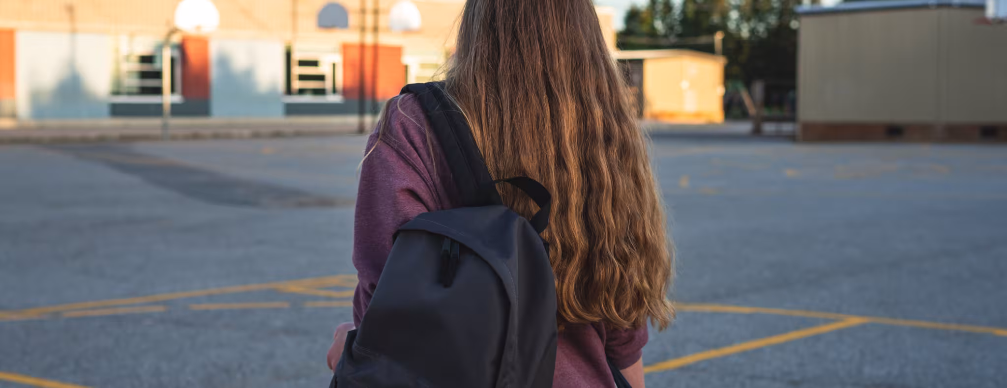 Teen girl in school parking lot, back of her