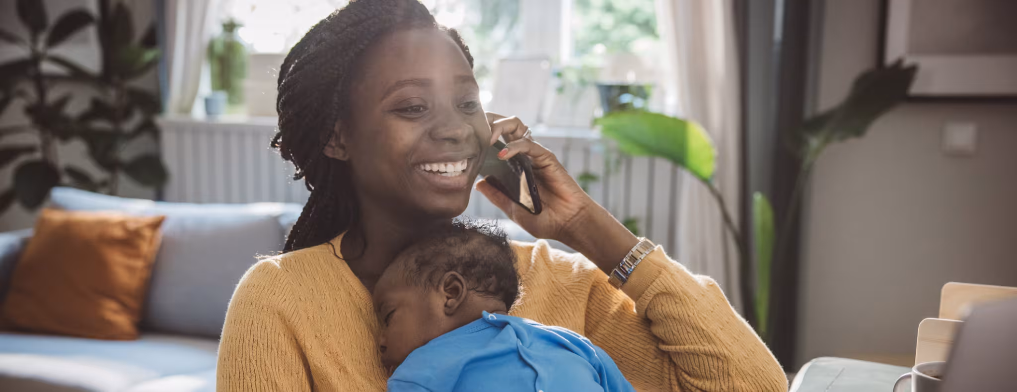 Young mother holding her baby son in arms while on her phone
